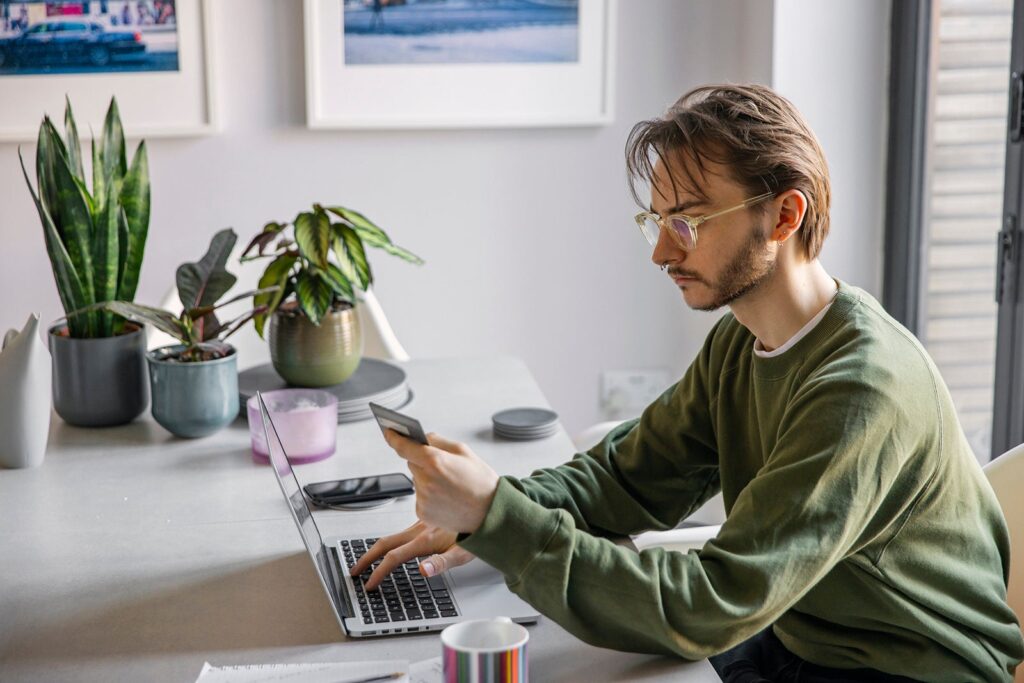 A person using a computer while holding a credit card